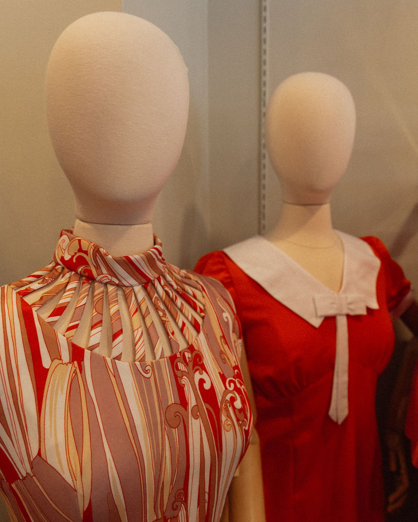 Two mannequins wearing red and patterned tops against a neutral background