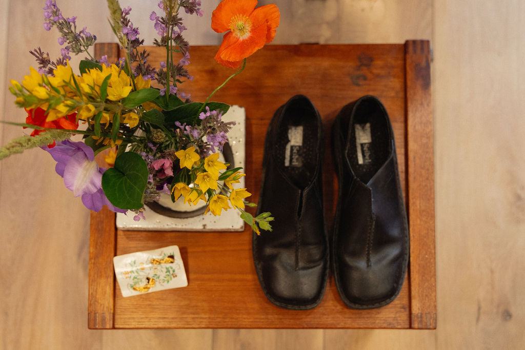 Pair of black shoes on a wooden surface with a bouquet of flowers and cards.